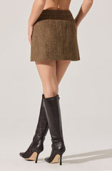 A woman is wearing a high-waisted, below-the-knee skirt with a brown and beige herringbone pattern. She is also wearing knee-high black leather boots with pointed toes and stiletto heels.