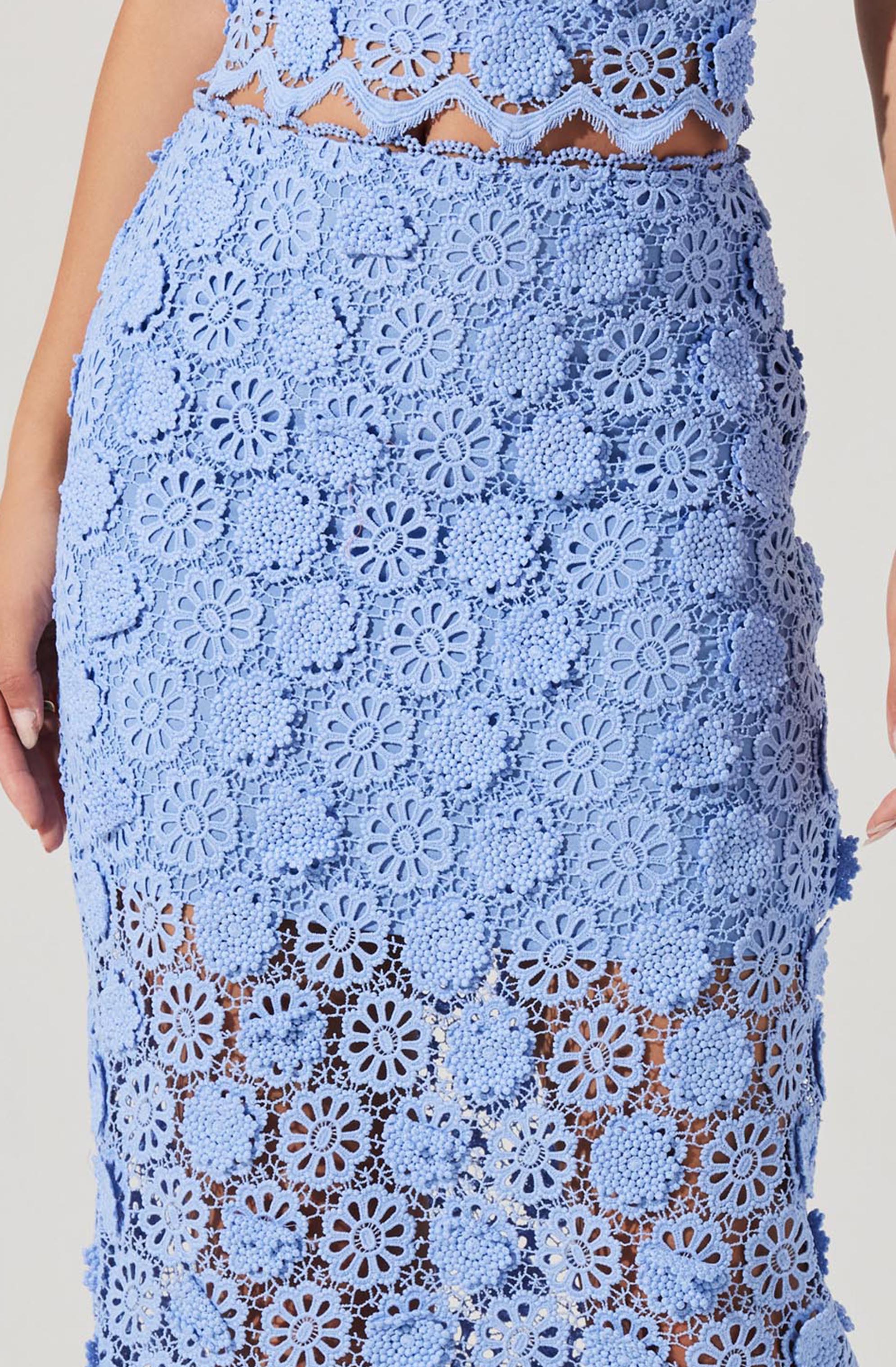 A person is wearing a two-piece outfit made of light blue lace fabric with floral cutout patterns. The top is a crop top with a scalloped edge and large flower motifs. The skirt is high-waisted, fitted, and features a sheer floral lace design with similar flower motifs, revealing a glimpse of skin beneath.