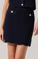 A woman is wearing a matching navy blue textured outfit consisting of a sleeveless top and a skirt. The fabric features horizontal, wavy ribbing. The top has decorative buttons with a pearl-like center and a ring of small rhinestones, as does the skirt, which also has small decorative fabric tabs near the waist with similar buttons.