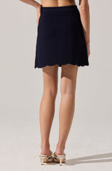 A woman is wearing a navy blue skirt with a textured, horizontal zigzag pattern and scalloped hemline, paired with beige high heels featuring decorative embellishments.