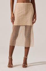 A woman is wearing a beige, high-waisted skirt with a fitted, opaque top portion and a see-through, sheer lower portion decorated with small, sparkling embellishments. She is also wearing strappy beige high-heeled sandals.