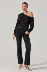 A woman is wearing a black off-the-shoulder blouse with long sleeves, adorned with small white polka dots. She pairs it with high-waisted, black jeans and silver high-heeled shoes.