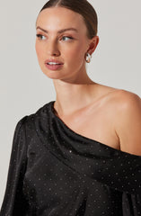 A woman is wearing an off-the-shoulder black dress adorned with small, sparkling silver dots throughout.