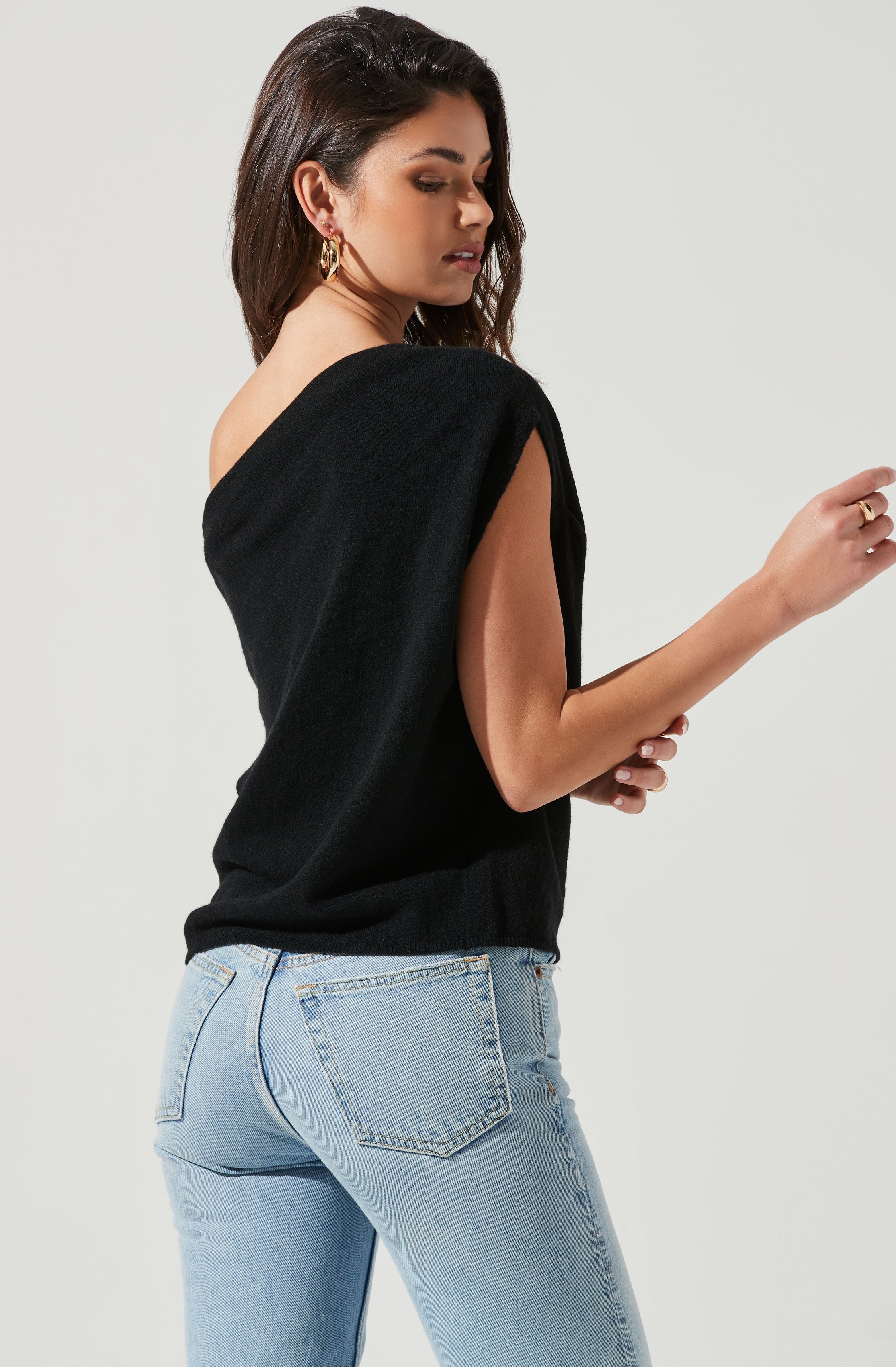 A woman is wearing a black sleeveless top with a wide shoulder cut, paired with light blue high-waisted jeans.