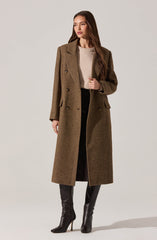 A woman is wearing a long, brown, double-breasted wool coat with a tailored fit, wide lapels, and flap pockets. Underneath, she has on a light beige knit sweater. She pairs this with black pants and black high-heeled knee-high boots.