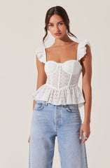 A woman is wearing a white eyelet top with ruffled shoulder straps, a sweetheart neckline, and a gathered, ruffled hem. The top has a fitted bust with vertical seam details and a peplum style that flares out at the waist. She pairs the top with light-wash, high-waisted jeans.