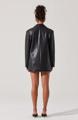 The person is wearing a black leather blazer with a tailored fit. The blazer is long, extending to the upper thighs. They are also wearing black pointed-toe high heels.