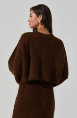 A woman is wearing a dark brown, fuzzy, long-sleeved sweater and a matching skirt. She has accessorized with large gold hoop earrings and a chunky gold chain necklace.