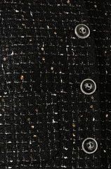 Close-up of a black textured fabric with a woven pattern, featuring three large silver buttons with an anchor emblem. The fabric appears to be part of a garment, possibly a blazer or coat, with a decorative, classic style.