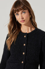 The woman is wearing a black, textured, long-sleeve cardigan with a round neckline, featuring a row of gold buttons down the front.