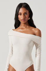 A woman is wearing a white, off-the-shoulder bodysuit with long sleeves. The fabric appears smooth and fitted, creating a sleek silhouette.