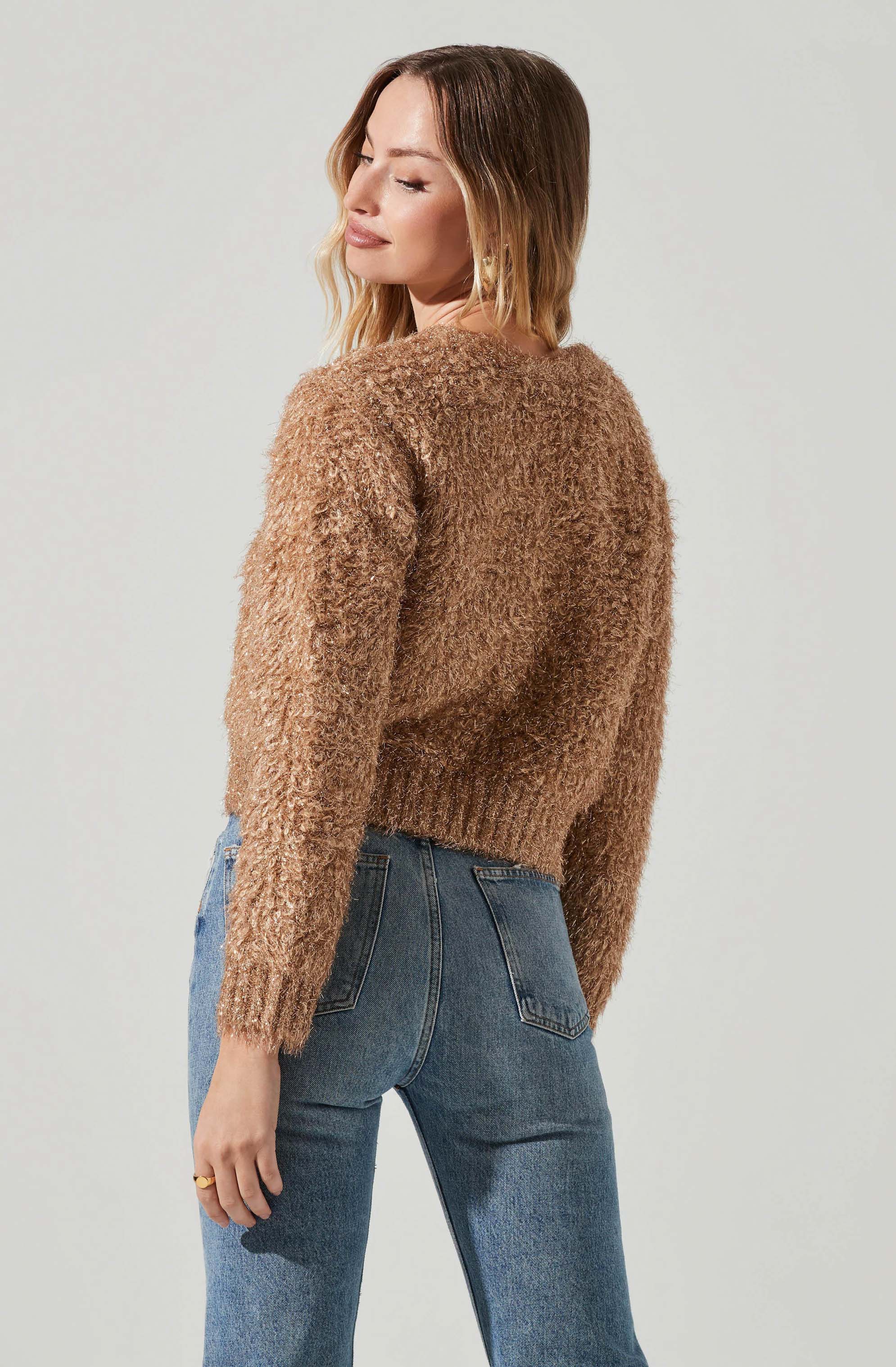 A woman is wearing a cozy, textured brown fuzzy sweater with long sleeves and a ribbed hem, paired with high-waisted blue jeans.