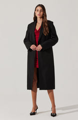A woman is wearing a long black coat over a red dress with a gathered or ruched bodice. She is also wearing black high heels with decorative embellishments on the toes.
