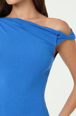 A woman wearing a bright blue, off-the-shoulder top with a knot detail on the right shoulder. The fabric appears to be smooth and slightly stretchy, fitting snugly. The top has a layered, draped design across the neckline.