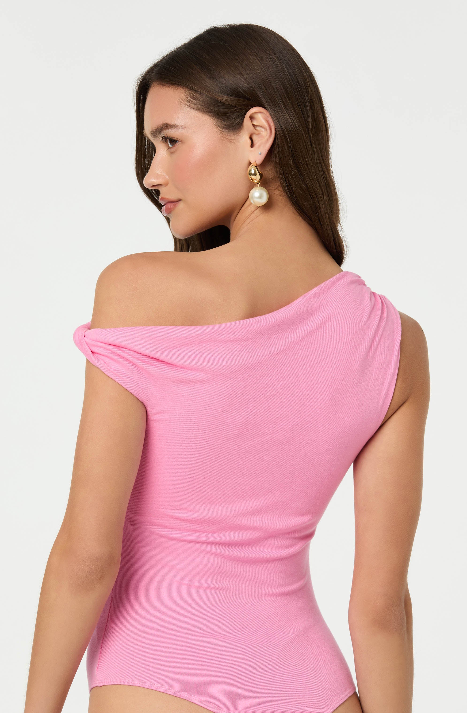 A woman is wearing a pink, form-fitting off-the-shoulder top with gathered fabric at the shoulder.