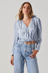 A woman is wearing a light blue satin cropped hoodie with long sleeves and a drawstring hood, paired with high-waisted, light-wash jeans.