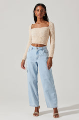 A woman is wearing a long-sleeved, textured, off-white cropped sweater with a square neckline. She pairs it with light-wash, high-waisted, wide-leg jeans and strappy high-heeled sandals.