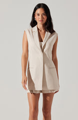 A woman is wearing a sleeveless, beige, tailored vest with lapels and two front pockets. She has paired it with matching beige shorts.