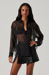 A woman wearing a sheer black button-up shirt with long sleeves and a classic collar. She is also wearing a black leather mini skirt with pleats and side slits.