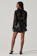 A woman is wearing a sheer black long-sleeve blouse with a collar, paired with a black leather mini skirt. She is also wearing black high-heeled sandals.