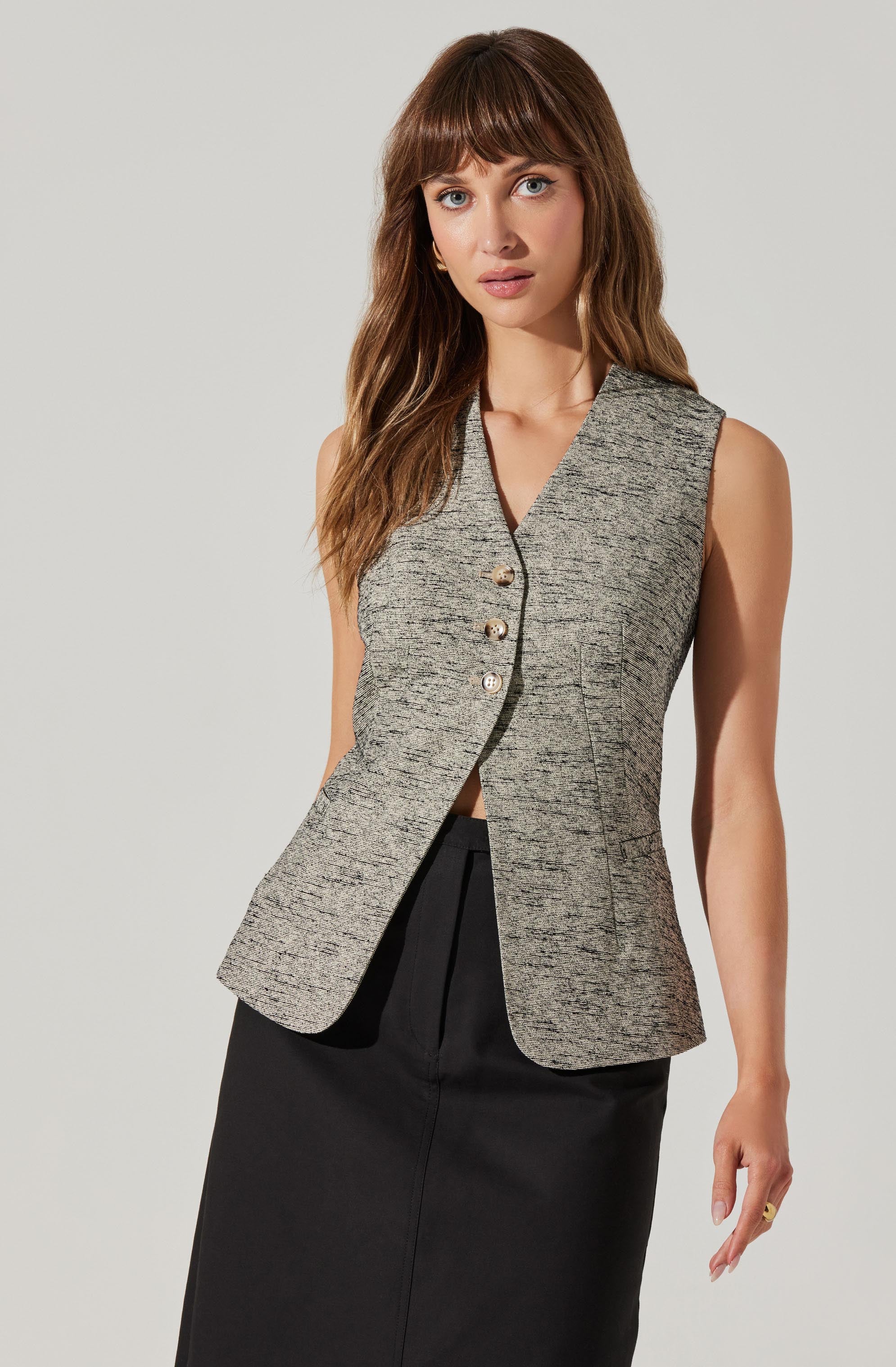 A woman is wearing a sleeveless, tailored, gray textured vest with a V-neckline and four decorative buttons down the front. The vest is fitted at the waist and flares slightly at the hips. She is also wearing a black high-waisted skirt.