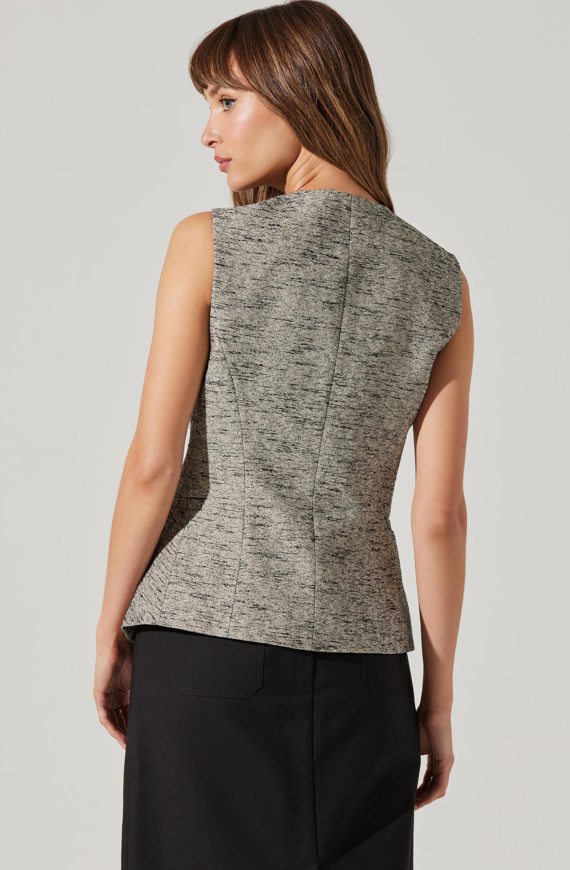 A woman is wearing a sleeveless, fitted, sleeveless top with a textured, gray fabric featuring a heathered pattern. The top has a seam running vertically down the back and a rounded neckline. She pairs it with a black skirt.