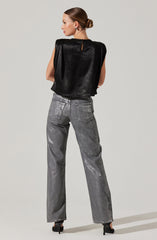 A woman is wearing a sleeveless black top with a shiny, textured fabric and a small keyhole opening at the back. She pairs it with high-waisted, loose-fitting gray jeans that have a faded, slightly distressed look. The outfit is completed with black high-heeled shoes.