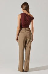 The image shows a woman wearing a sleeveless, dark red, one-shoulder top with a gathered detail on the shoulder. She is also dressed in high-waisted, beige, wide-leg trousers with two back pockets featuring button closures.