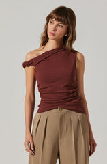 A woman is wearing a sleeveless, asymmetrical, one-shoulder maroon top with a knot detail on the shoulder. She pairs it with high-waisted, beige pleated pants.