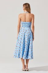 A woman is wearing a light blue halter top with elastic shirring at the back and a matching high-waisted, full-length skirt. The skirt features a brown polka dot pattern throughout. She is also wearing white high-heeled shoes.