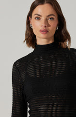 A woman is wearing a black, long-sleeved, high-neck top with a textured, open-knit pattern.