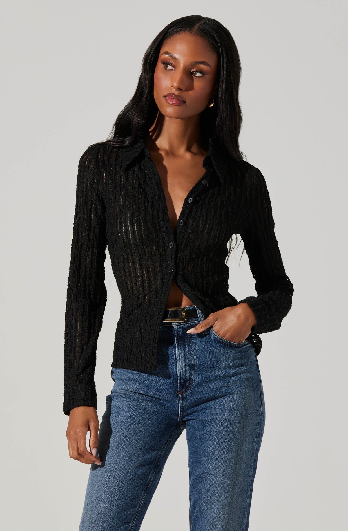 A woman is wearing a black, long-sleeved, button-up cardigan with a textured, ribbed pattern. She pairs it with high-waisted blue denim jeans.
