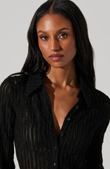A woman with long, straight black hair is wearing a fitted black button-up shirt with a textured, semi-sheer striped pattern. The shirt has a collar and appears to be made of a lightweight, slightly see-through fabric.