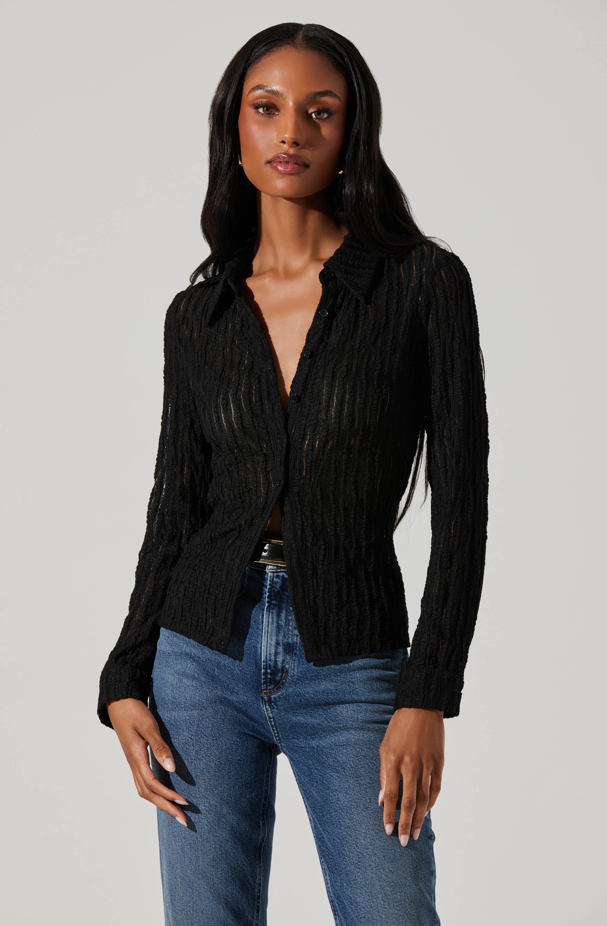 A woman is wearing a long-sleeved, black, open-knit sweater with a collar and button-down front, paired with blue jeans.