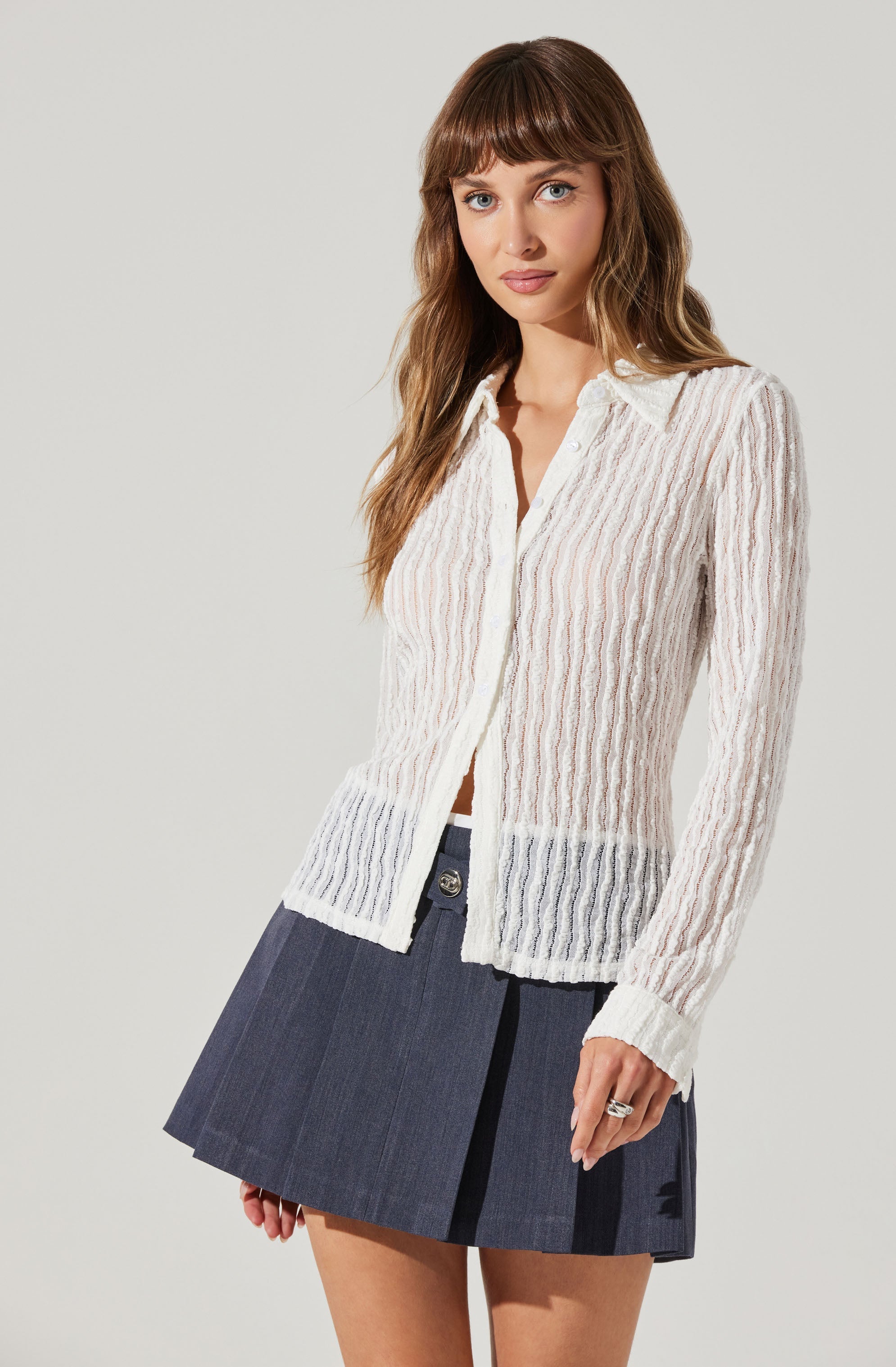 A woman is wearing a long-sleeved, cream-colored, ribbed cardigan with an open front and a collared neckline. The cardigan has vertical stripes and is slightly sheer, showing a hint of the shirt underneath.