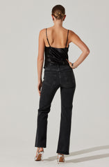 A woman is wearing a black satin camisole with thin spaghetti straps and a pair of high-waisted, straight-leg black jeans. She is also wearing white high-heeled shoes.