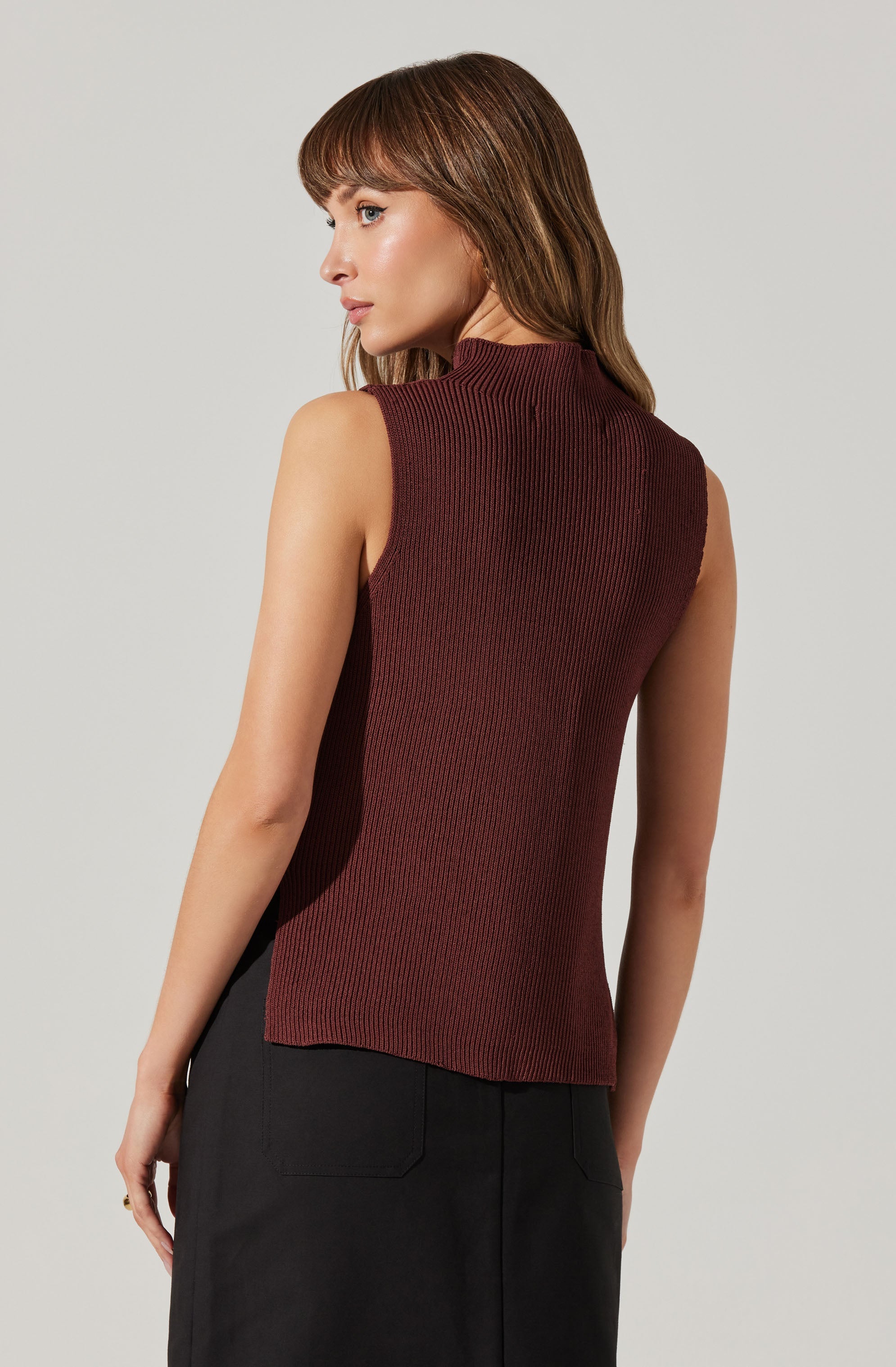 A woman is wearing a sleeveless, high-neck, ribbed top that is maroon with subtle black vertical lines. She is also wearing black pants.