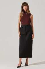 A woman is wearing a sleeveless, high-neck, ribbed burgundy top paired with a high-waisted, black, ankle-length skirt. She completes her outfit with black pointed-toe high heels.
