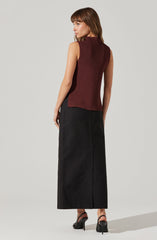 A woman is wearing a sleeveless, ribbed, high-neck top in a dark burgundy color and a long, black, ankle-length skirt. She is also wearing black high-heeled sandals with ankle straps.