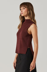 A woman is wearing a sleeveless, high-neck, ribbed knit top in a deep burgundy color, paired with black pants. The top has a slightly widened armhole and side slits at the hem.