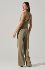 A woman is wearing a sleeveless, olive-green top with a fitted waist and a zipper detail on the back. She is also dressed in high-waisted, wide-leg beige trousers with back pockets.