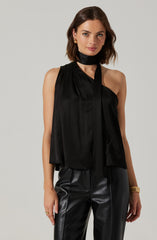 A woman is wearing a sleeveless black top with a high neckline and an attached long tie that drapes down the front. She is also wearing black leather pants.