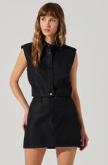 A woman is wearing a sleeveless black button-up shirt with a collar, paired with a black high-waisted skirt. The shirt has shoulder pads, giving it a structured appearance.