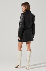 A woman is wearing a black jacket with leather sleeves and a black skirt. She has white knee-high boots with high block heels.