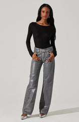 A woman is wearing a fitted black long-sleeve top with a round neckline, paired with high-waisted, loose-fitting metallic silver jeans. She is also wearing silver pointed-toe shoes.