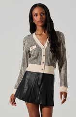 A woman is wearing a long-sleeved, button-up knit cardigan with a black and beige striped pattern, beige trim along the collar, button placket, sleeve cuffs, and hem. The cardigan features a small pocket on the left chest with matching striped fabric. She pairs the cardigan with a black pleated leather mini skirt.