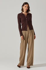 A woman is wearing a fitted, long-sleeved, ribbed brown cardigan with a collar and button-up front. She has paired it with high-waisted, wide-leg beige trousers.