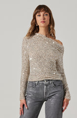 A woman is wearing a long-sleeved, off-the-shoulder top covered in silver glitter, giving it a sparkly and glamorous appearance. She pairs it with high-waisted, metallic gray jeans.
