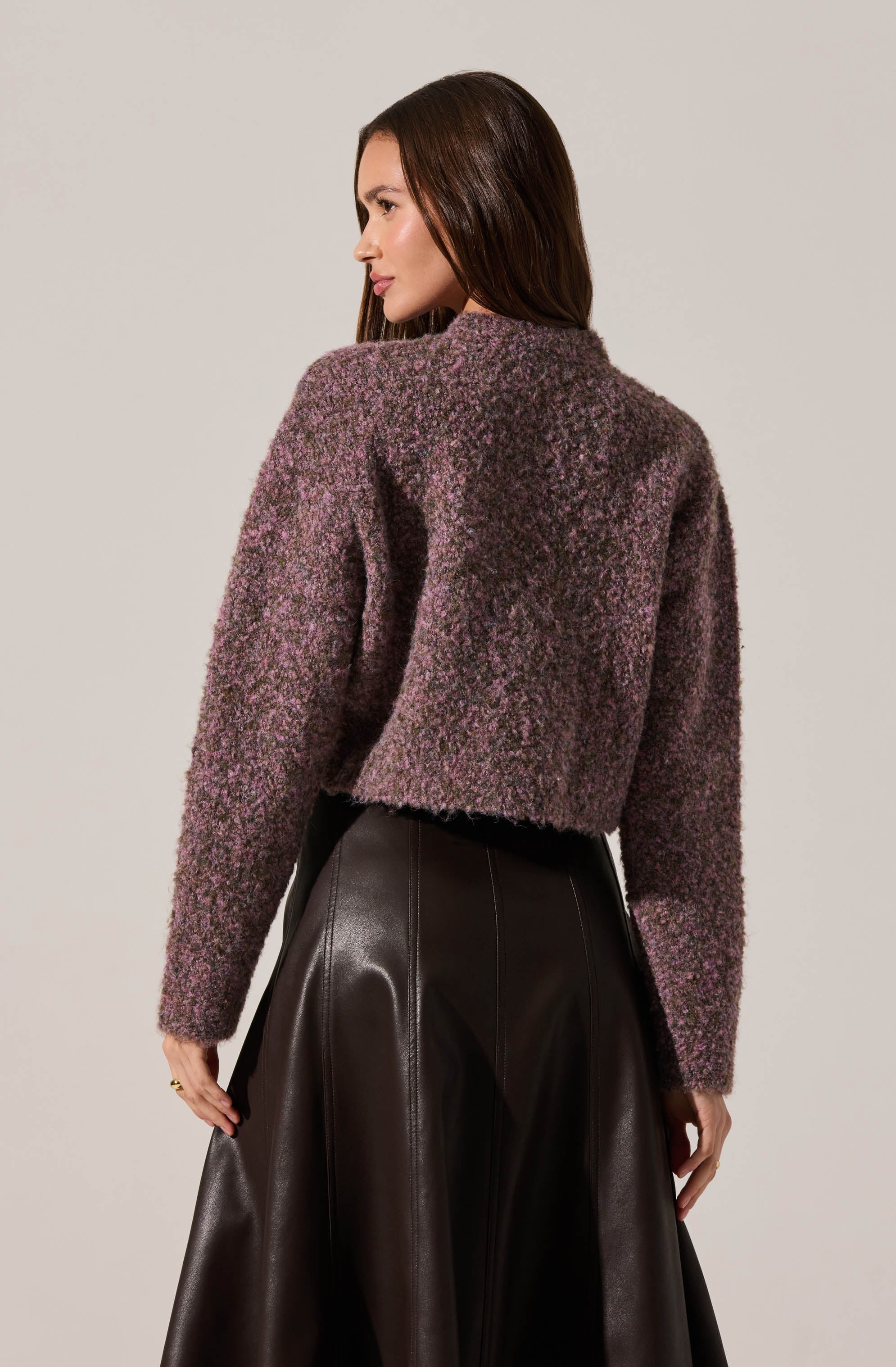 A woman is wearing a textured, fuzzy sweater in a mix of purple, pink, and brown tones. The sweater has a high neckline and long sleeves. She pairs it with a high-waisted, dark brown leather skirt that has a glossy finish.