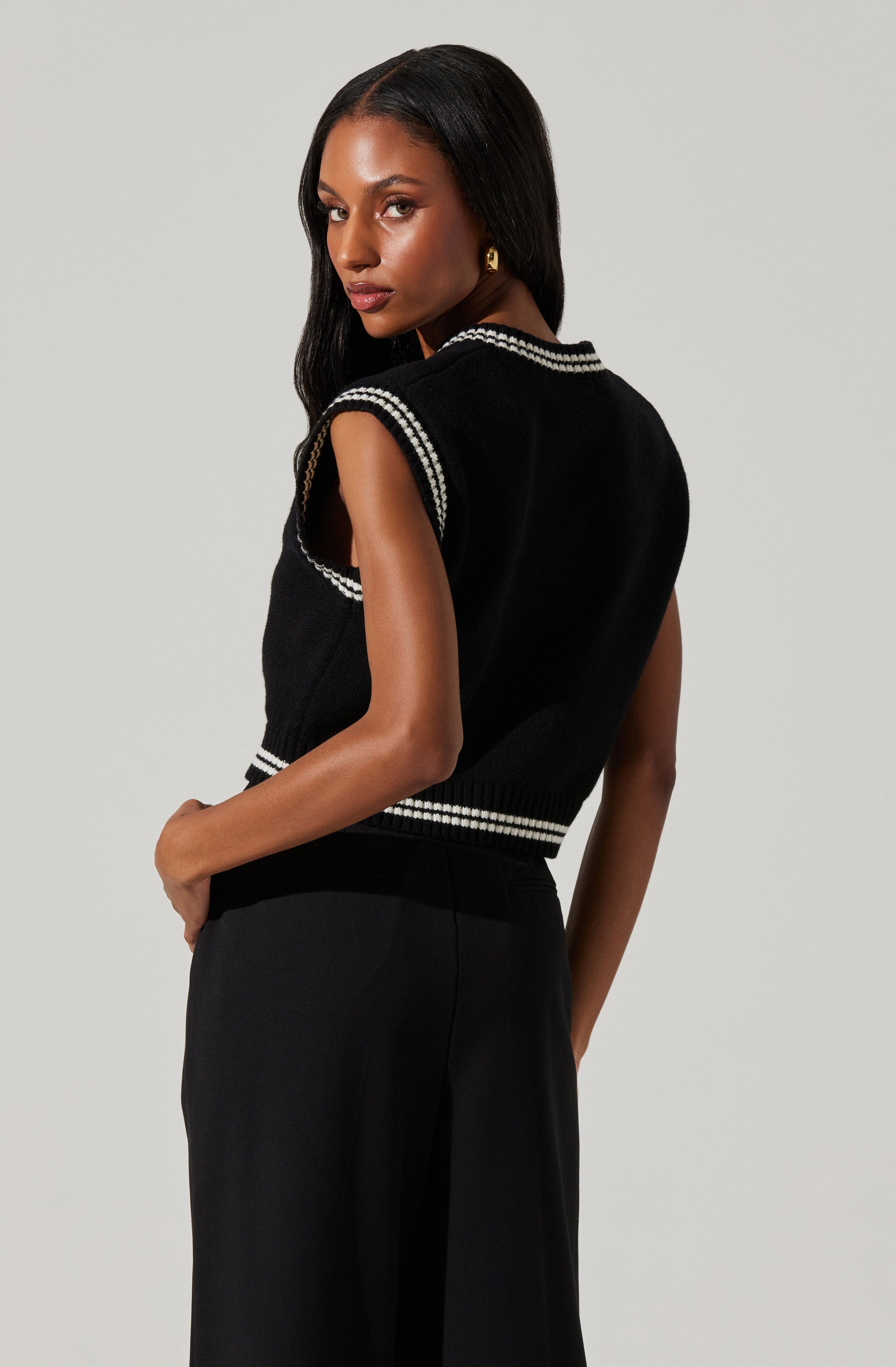 A woman is wearing a sleeveless black knit top with white stripe accents along the neckline, armholes, and hemline.